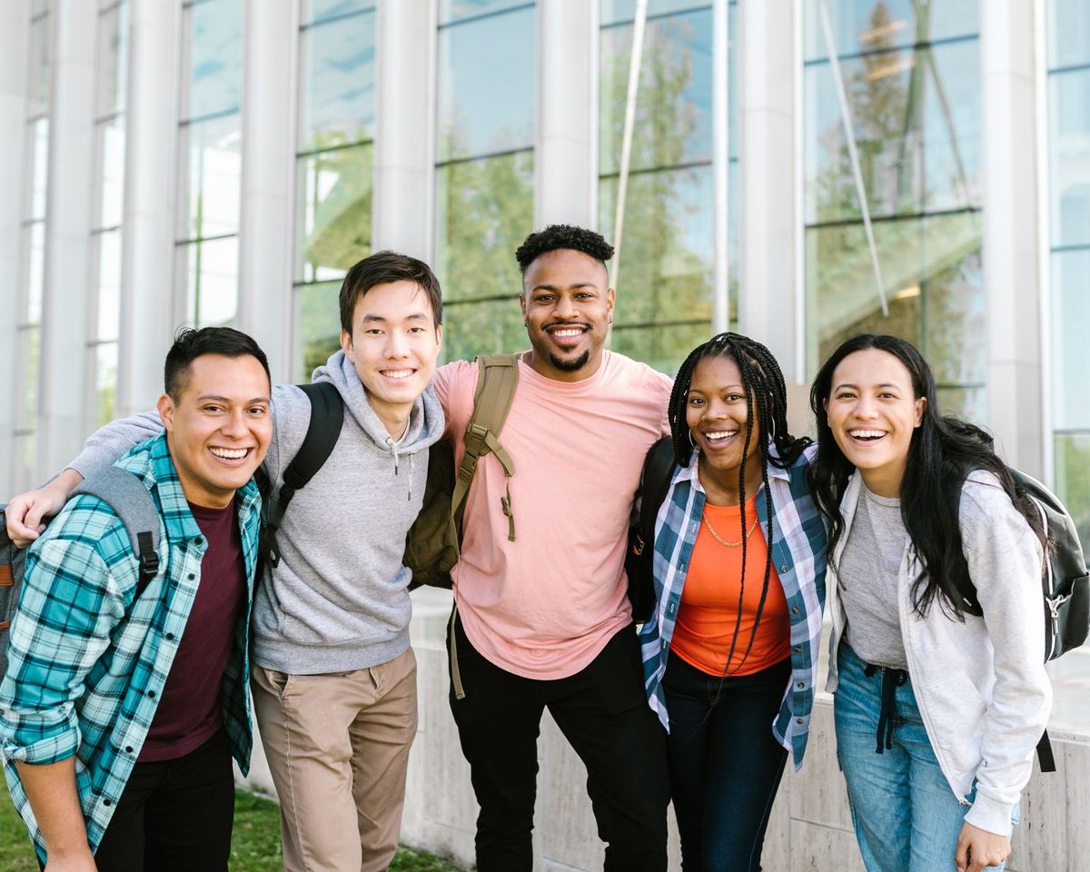 Five smiling college students standing together outside a campus building