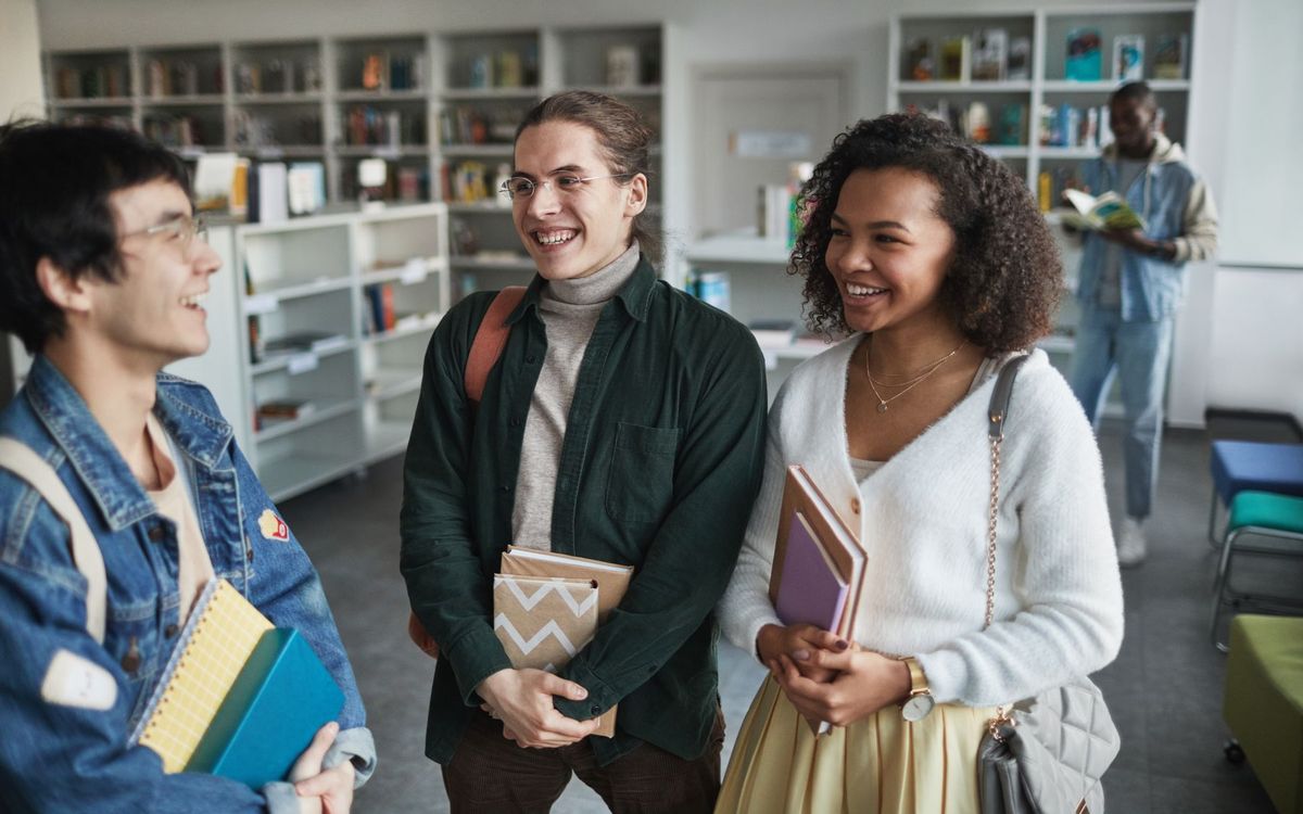 Three smiling students talking in a college library