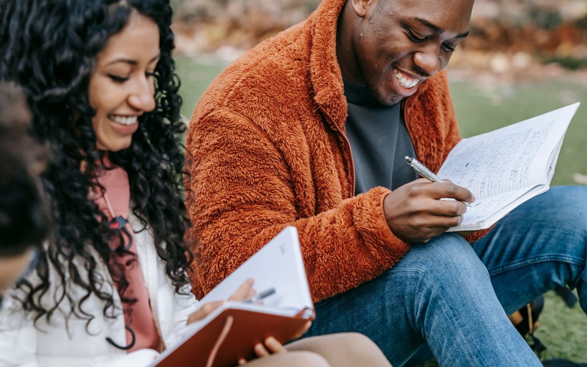 Two smiling students reading together on a campus lawn